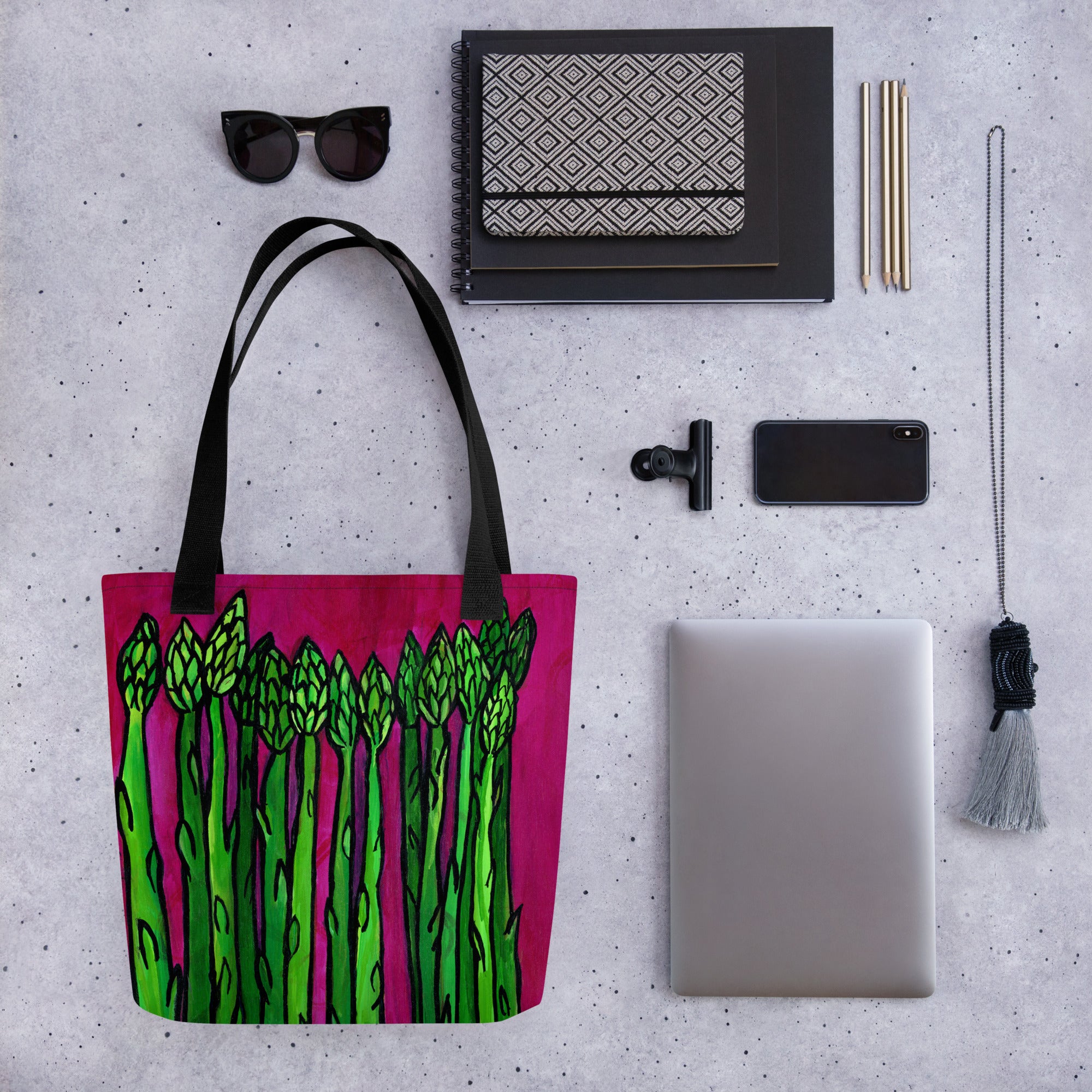 Asparagus tote bag shown with different items - sunglasses, notebooks, pencils, clip, phone, lanyard, and laptop
