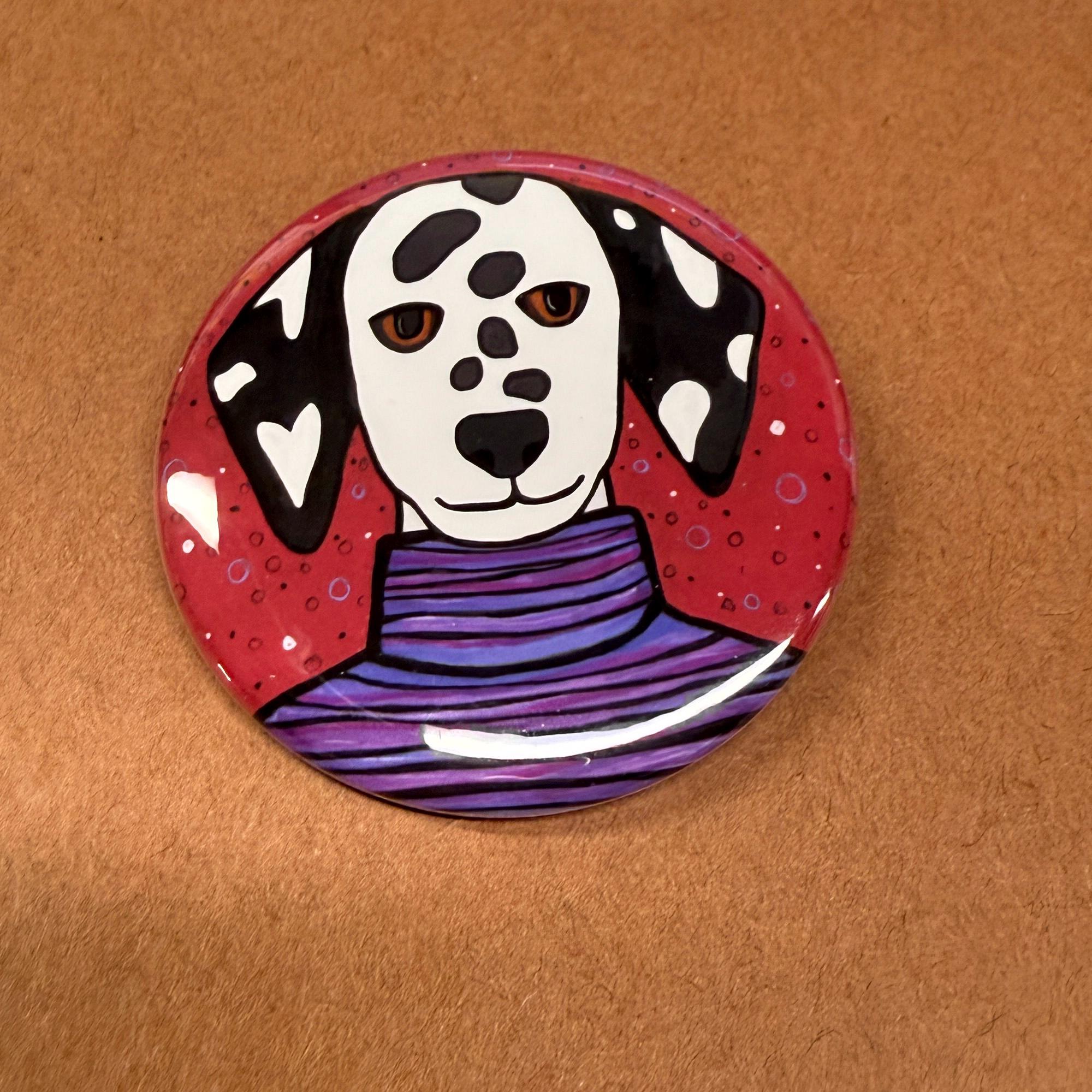 Dottie the Dalmatian is a round pin or magnet available in 2 sizes. She is shown on a brown background.