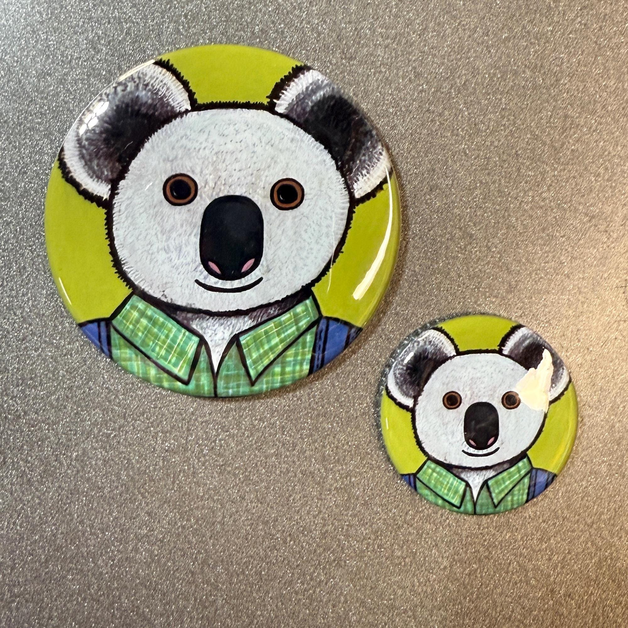 Two different sizes of buttons shown - 2.25 inch and 1.25 inch. Koala in green plaid shirt and blue overalls on a green background.