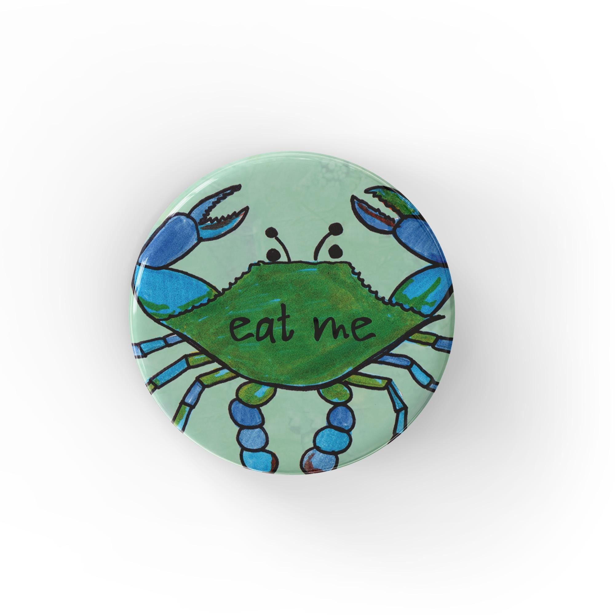 Light blue green button with a hand drawn blue crab with the words eat me on the center of its shell