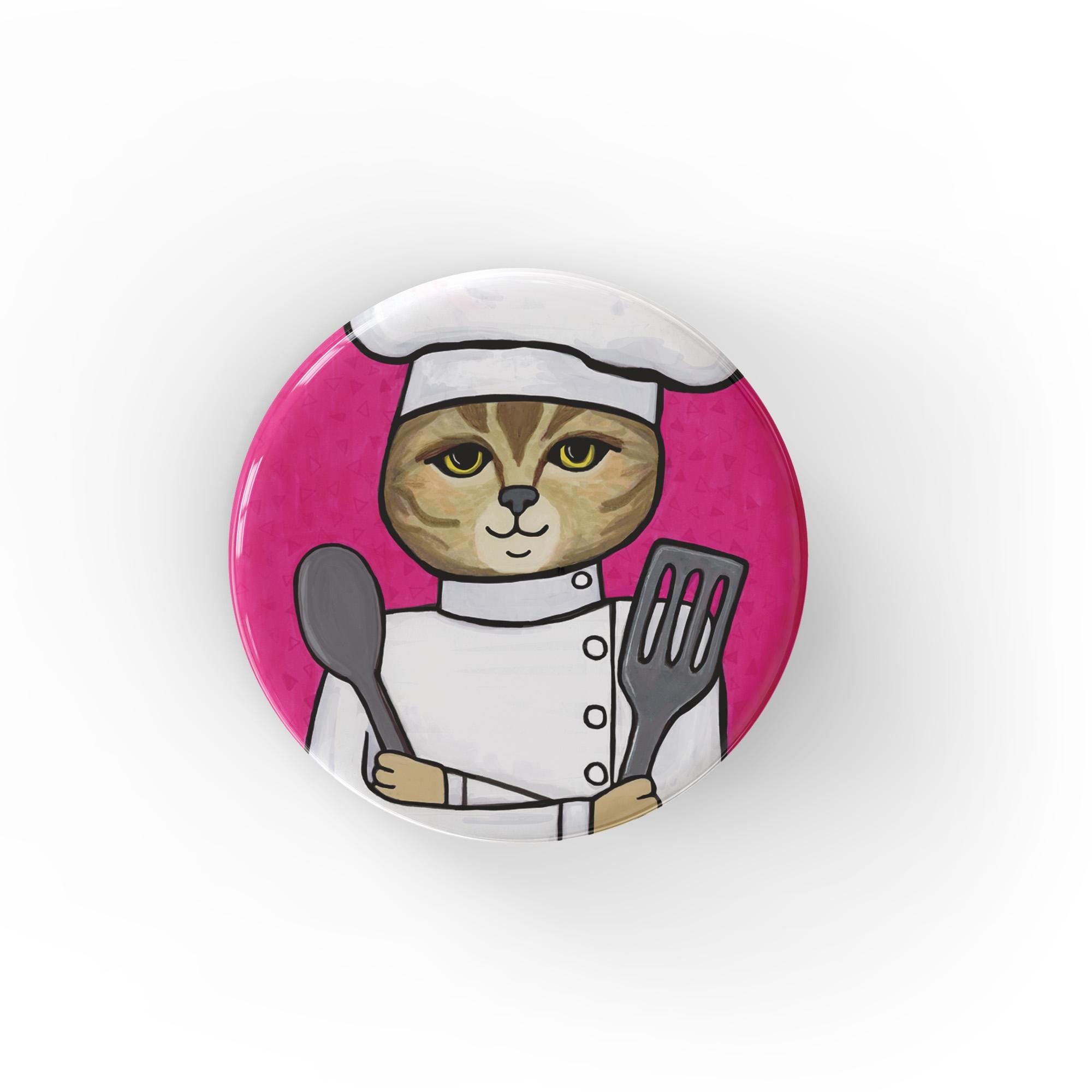 Round pink button with a hand drawn cat chef wearing chef's hat and jacket and holding a metal spoon and spatula. Available as a pin, magnet, or pocket mirror.