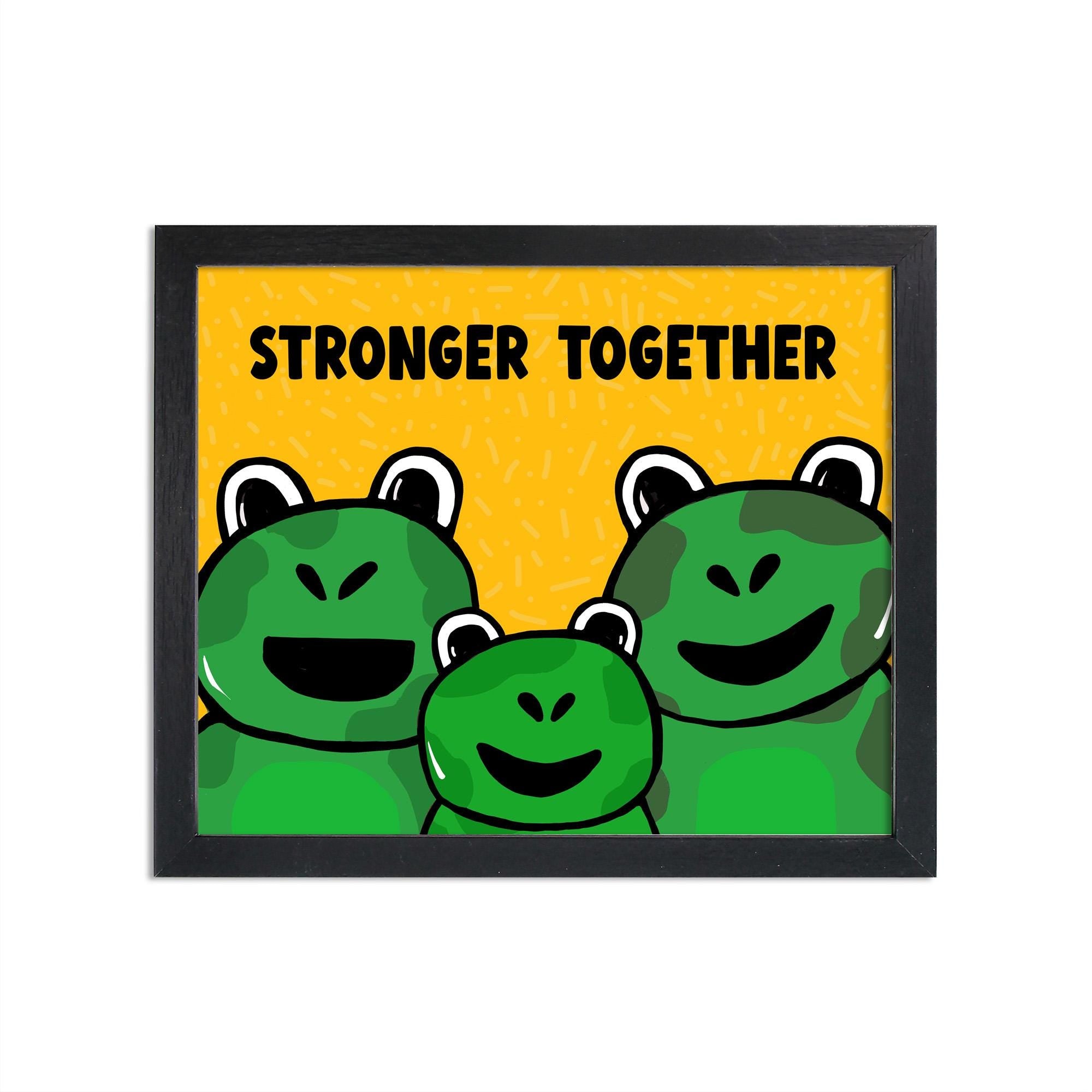 Stronger Together frog art print shown in a black frame. The image features 3 frogs - 2 adult, 1 child - on a yellow background with subtle dash dot texture and the words Stronger Together in a all caps black font.