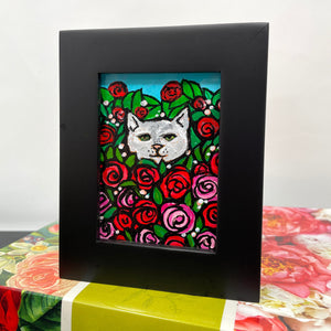 Rose Kitty II painting in black chunky frame sits on top of a flower book
