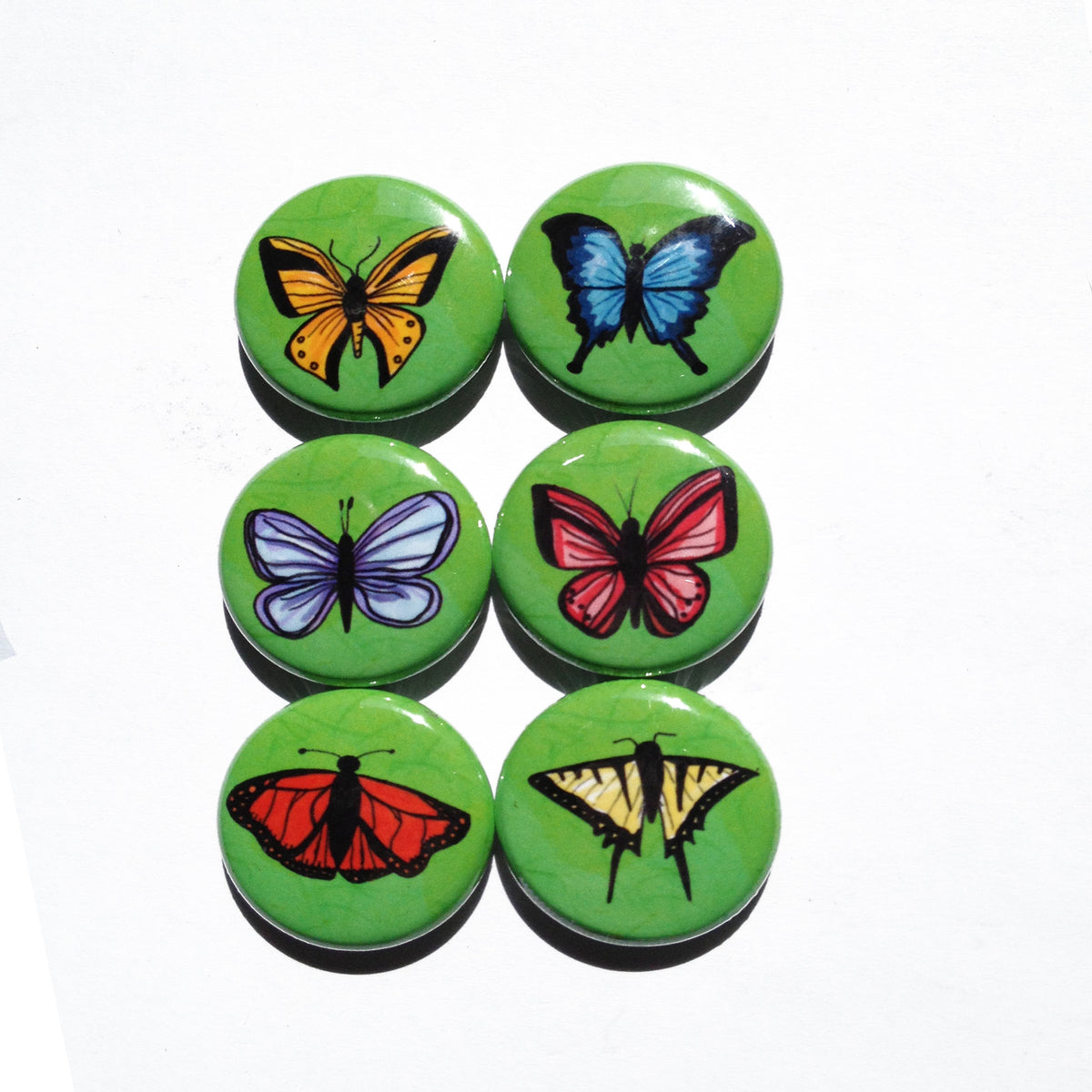 different color butterflies on round green buttons on a white background