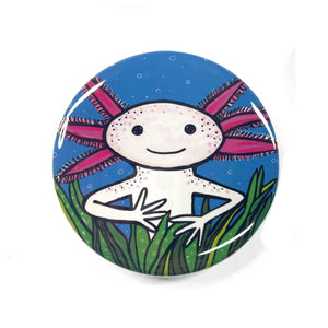 Axolotl magnet, pin, or pocket mirror. Smiling axolotl peering over grasses with blue water background with white bubbles.