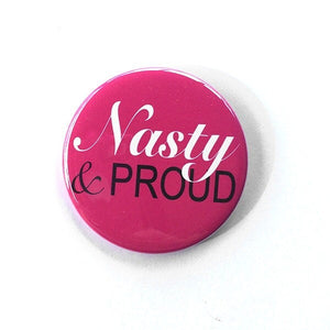 Round button with the words nasty in white cursive and proud in black sans serif font. Background is pink.