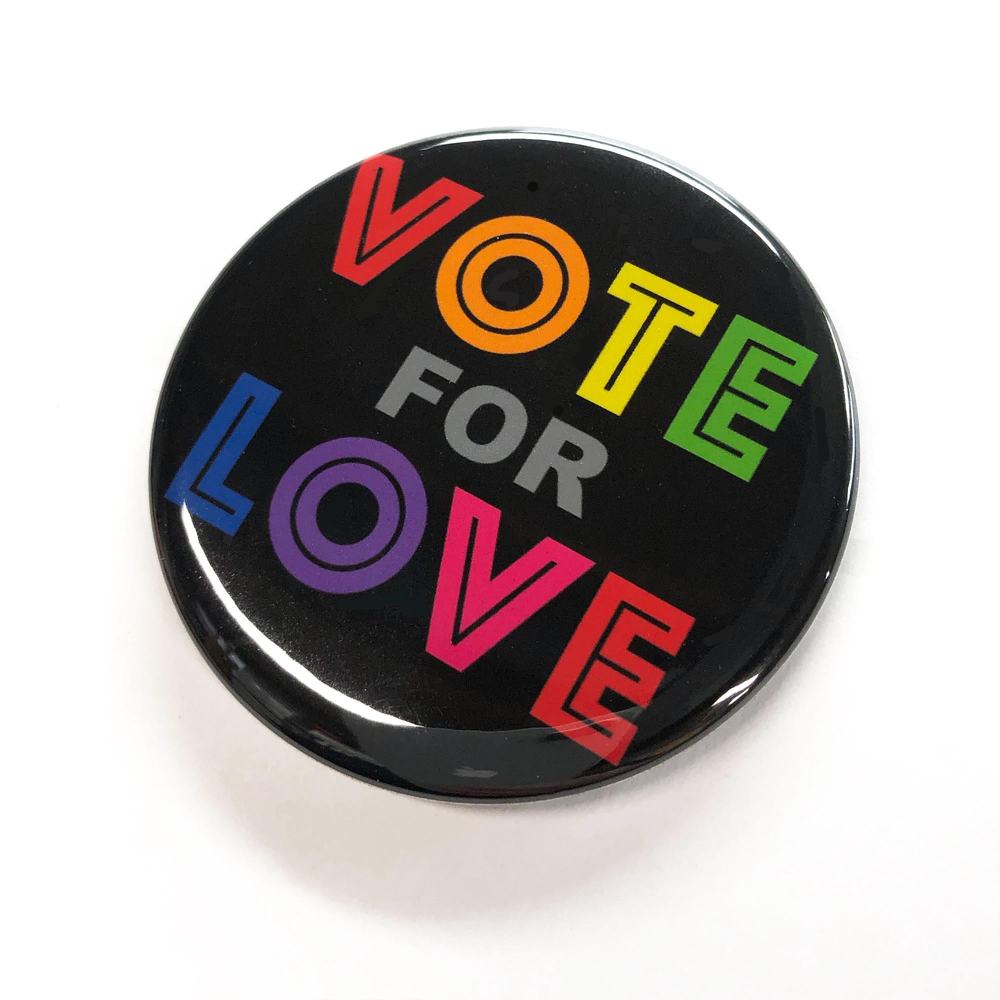 Side view of button. Black round button with the words Vote for Love in all caps and rainbow colors. Each letter is a different color.