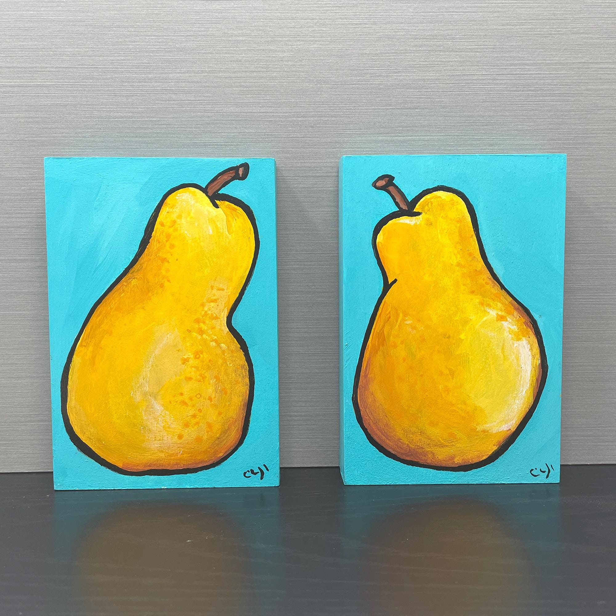 pair of acrylic pear paintings on black table with gray background - yellow pears on aqua background