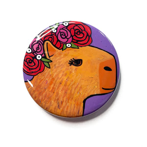 Round button with capybara wearing rose crown in shadees of pink and red on purple background