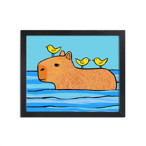 Image of Capybara Friend to All art print in black frame. Art features brown capybara swimming with two yellow birds on it's back and one bird on its head. Background is lighter blue.