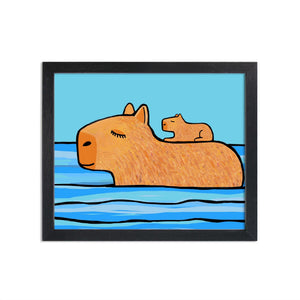 Capybara art print in black frame. Art features mother capybara with baby pup on her back as she swims through blue water with blue sky in the background.