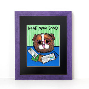 Ginger the Guinea Pig reading books with the saying Read More Books on the top of the art print. Shown in black mat and purple frame.