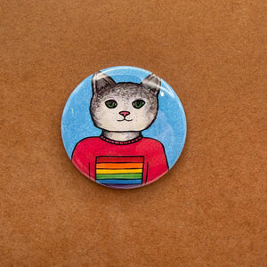 Round button with a gray and white cat in a pink tshirt with rainbow flag