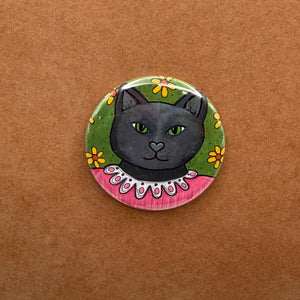 Round button with Jane the Black Cat in a pink dress on a green floral background