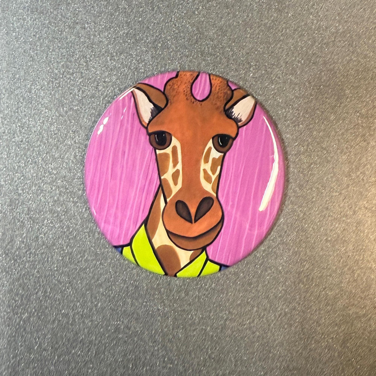 Round button of a giraffe in a bright green shirt on a pink striped background