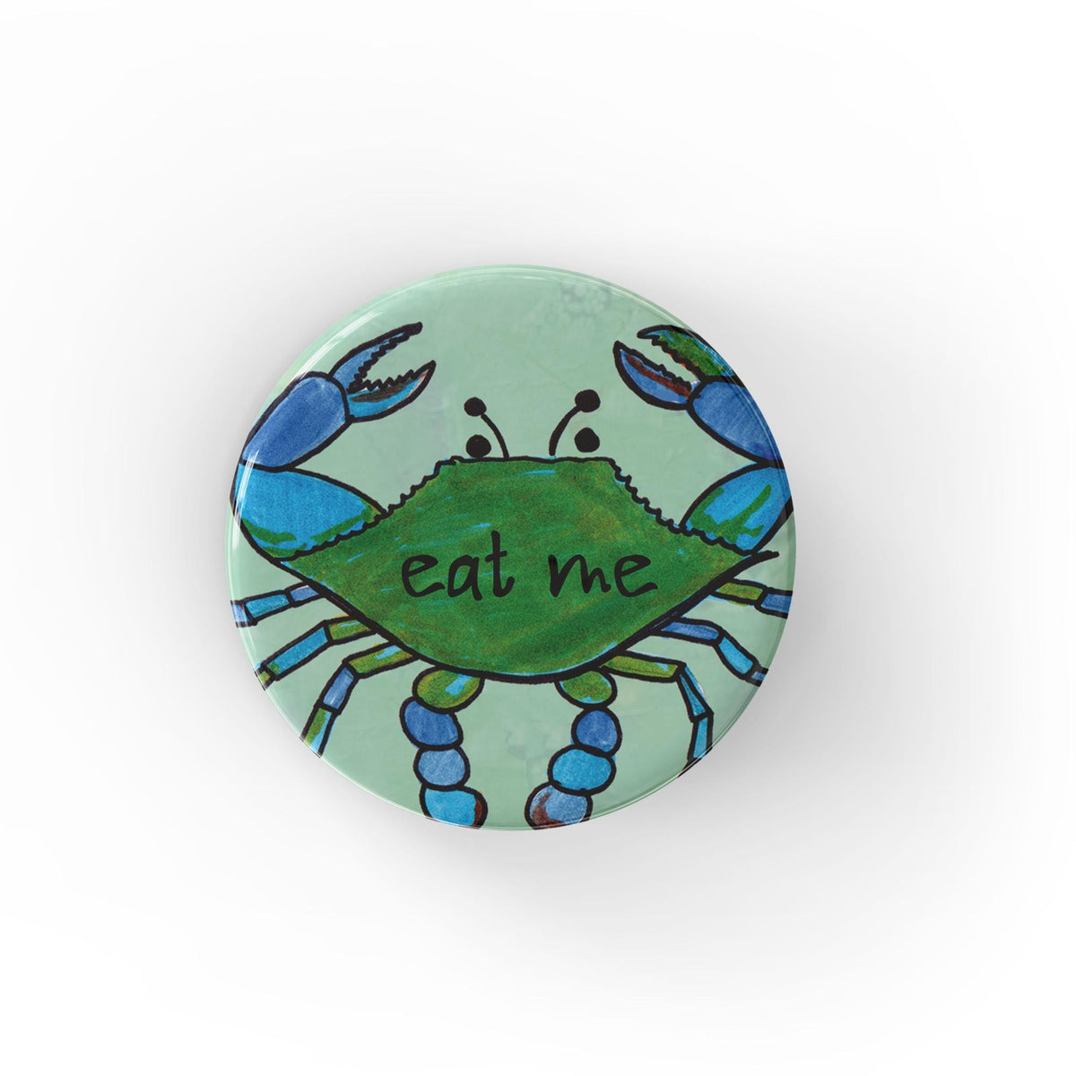 Light blue green button with a hand drawn blue crab with the words eat me on the center of its shell