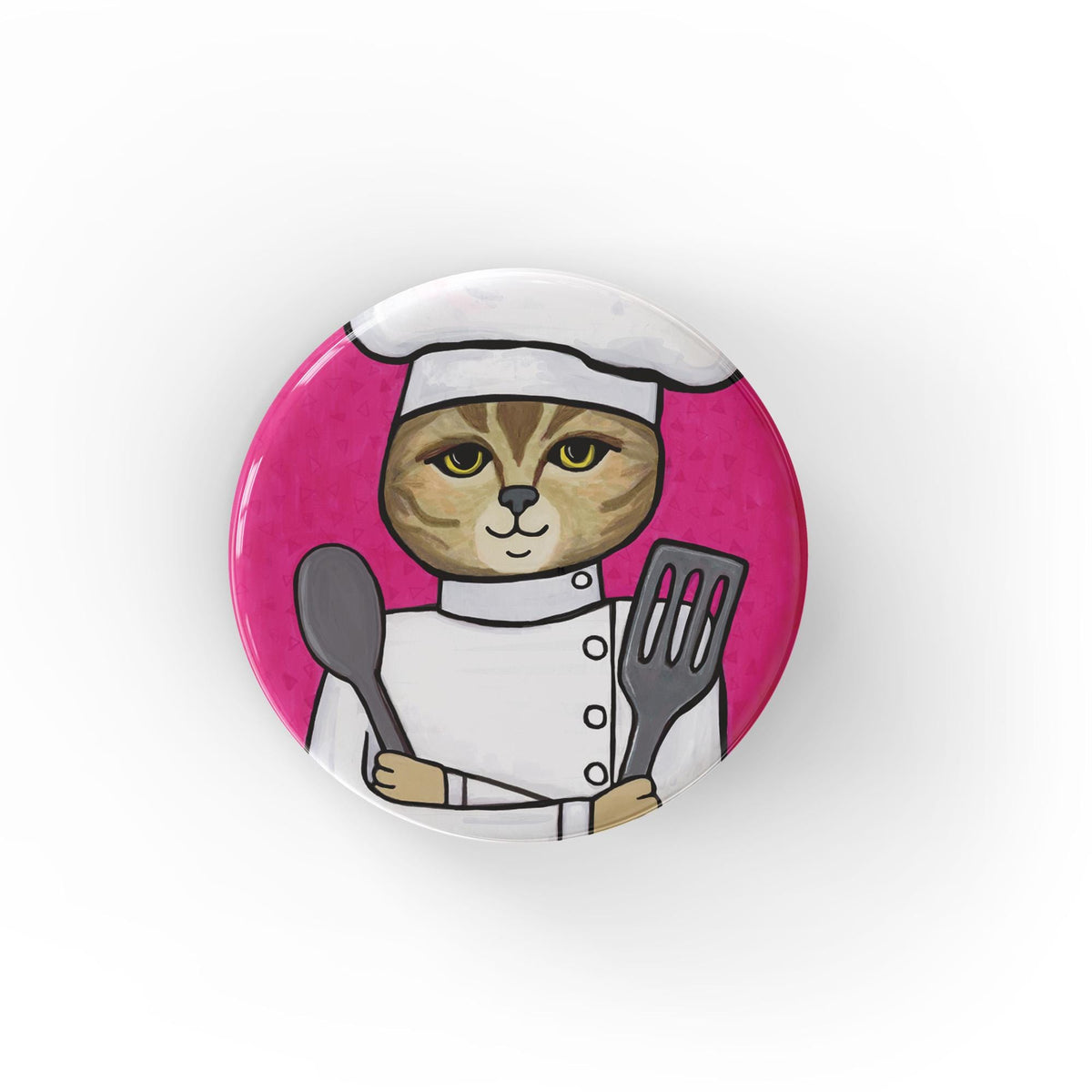 Round pink button with a hand drawn cat chef wearing chef&#39;s hat and jacket and holding a metal spoon and spatula. Available as a pin, magnet, or pocket mirror.
