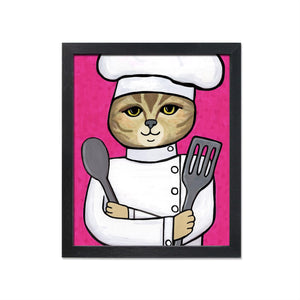 Cat Chef art print in a simple black frame. Art features an american shorthair cat in a chef&#39;s hat and jacket holding metal spoon and spatula on a pink background