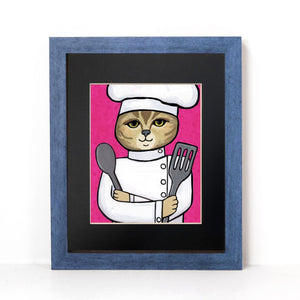 Cat Chef art print in a black mat and blue wood frame. Art features an american shorthair cat in a chef&#39;s hat and jacket holding metal spoon and spatula on a pink background