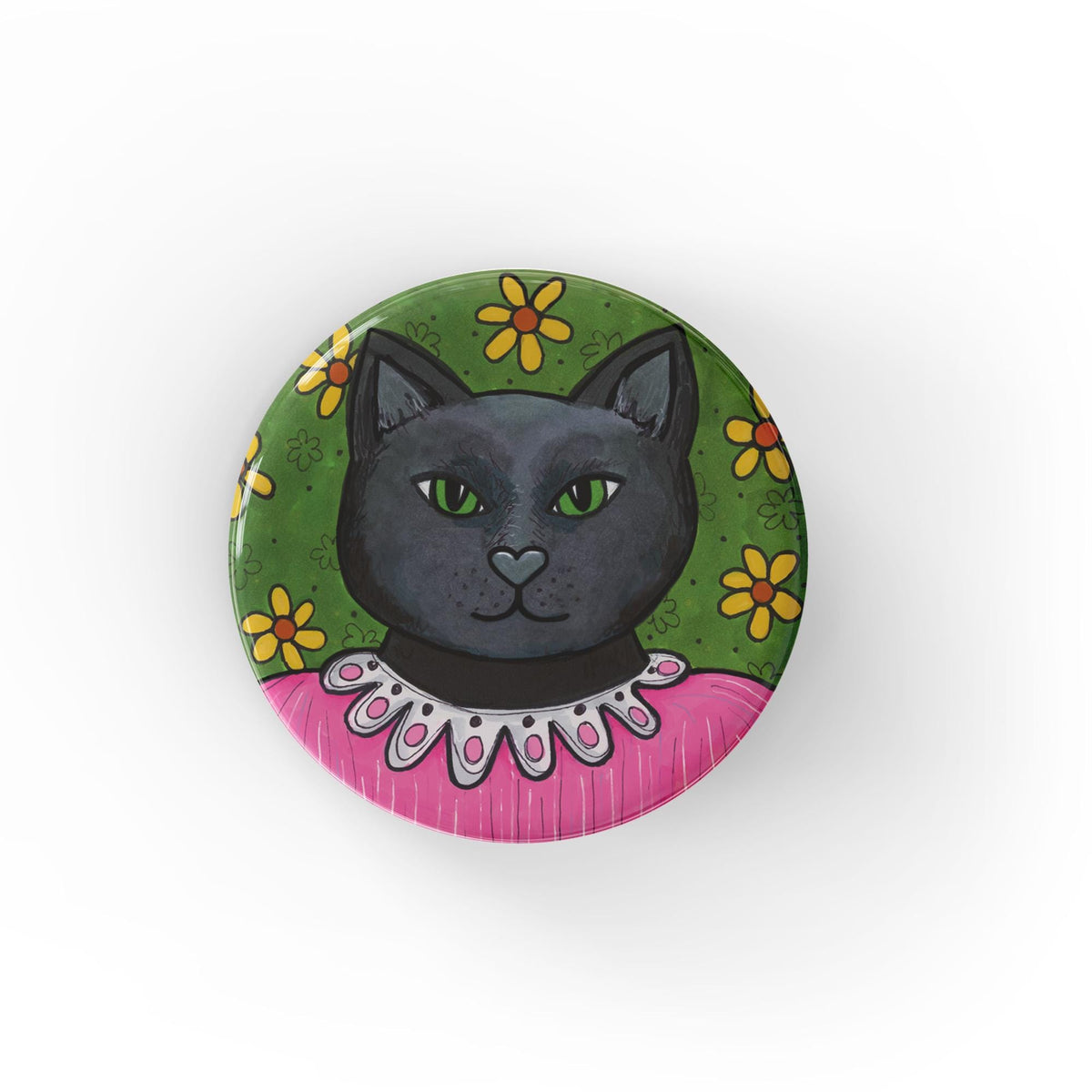 Round black cat pin back button or fridge magnet featuring a black cat in a frilly pink dress on a green background with yellow flowers.