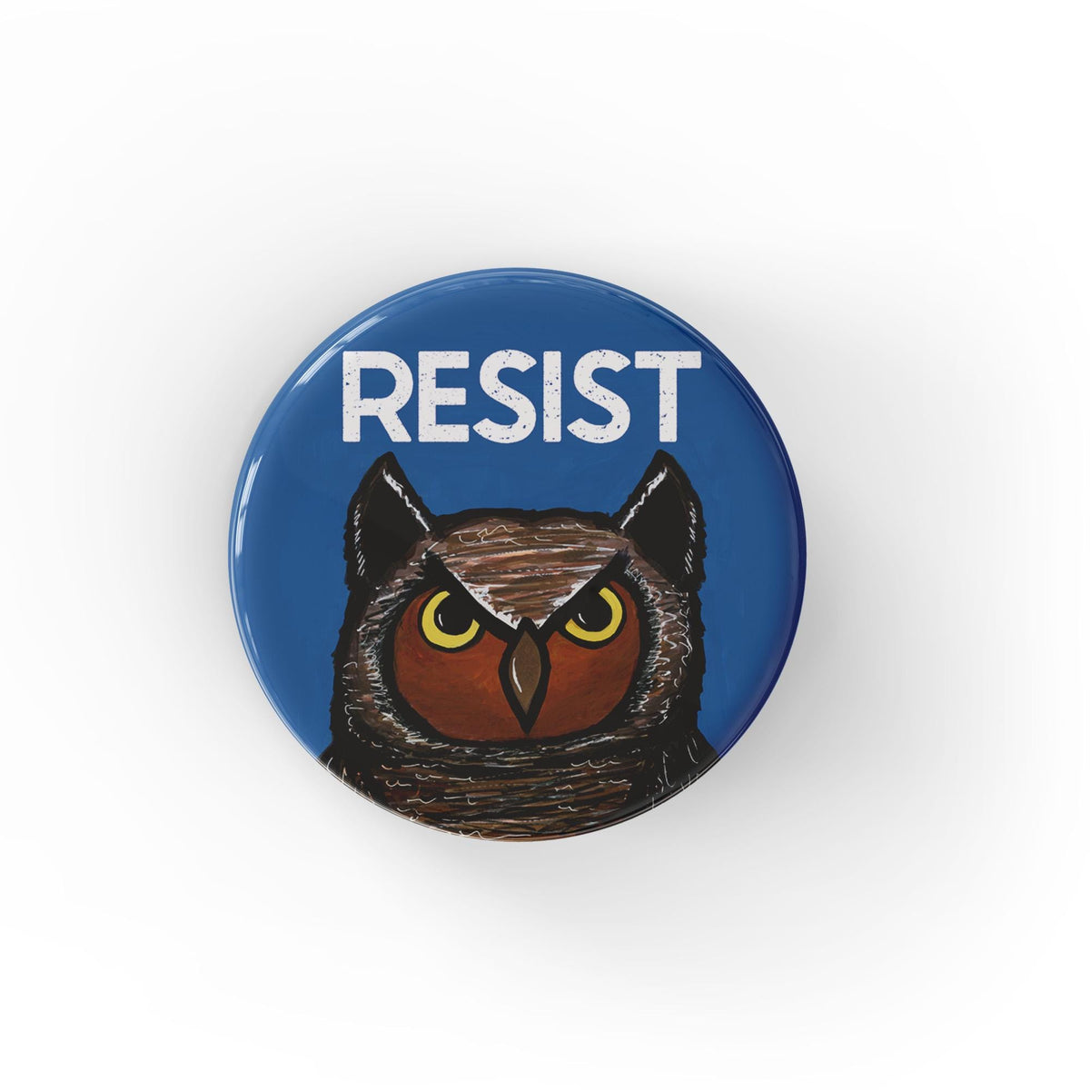 Round blue button with the word RESIST in white at the top and a hand drawn owl face on the lower half.