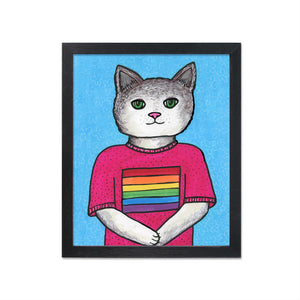 May include: Framed artwork featuring a cat with a gray head and green eyes. The cat wears a pink shirt with a rainbow stripe design. The background is light blue with a floral pattern. The frame is black.