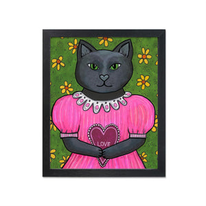 Jane the Black Cat art print in black frame - design features a black cat in a pink puffy dress holding a love heart. She stands against a green floral wall with yellow flowers.