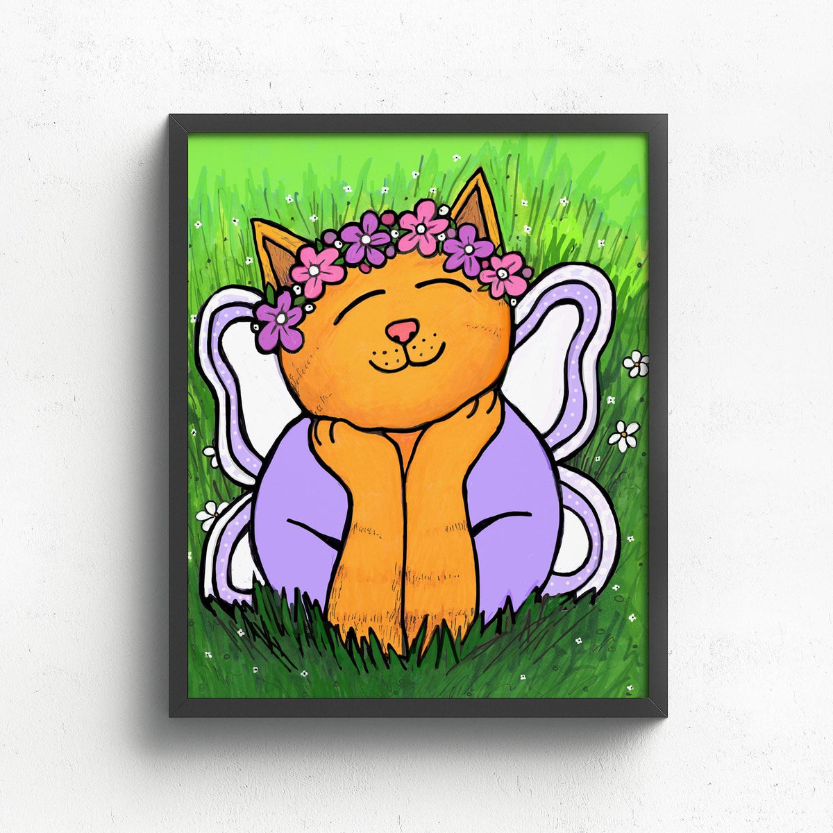 art print of Chloe the Cat Fairy shown in a black frame on a white wall. The yellow tabby cat in wearing purple and pink flower crown and purple shirt. She is laying in the grass with head resting on her hands and her white and purple wings behind her.