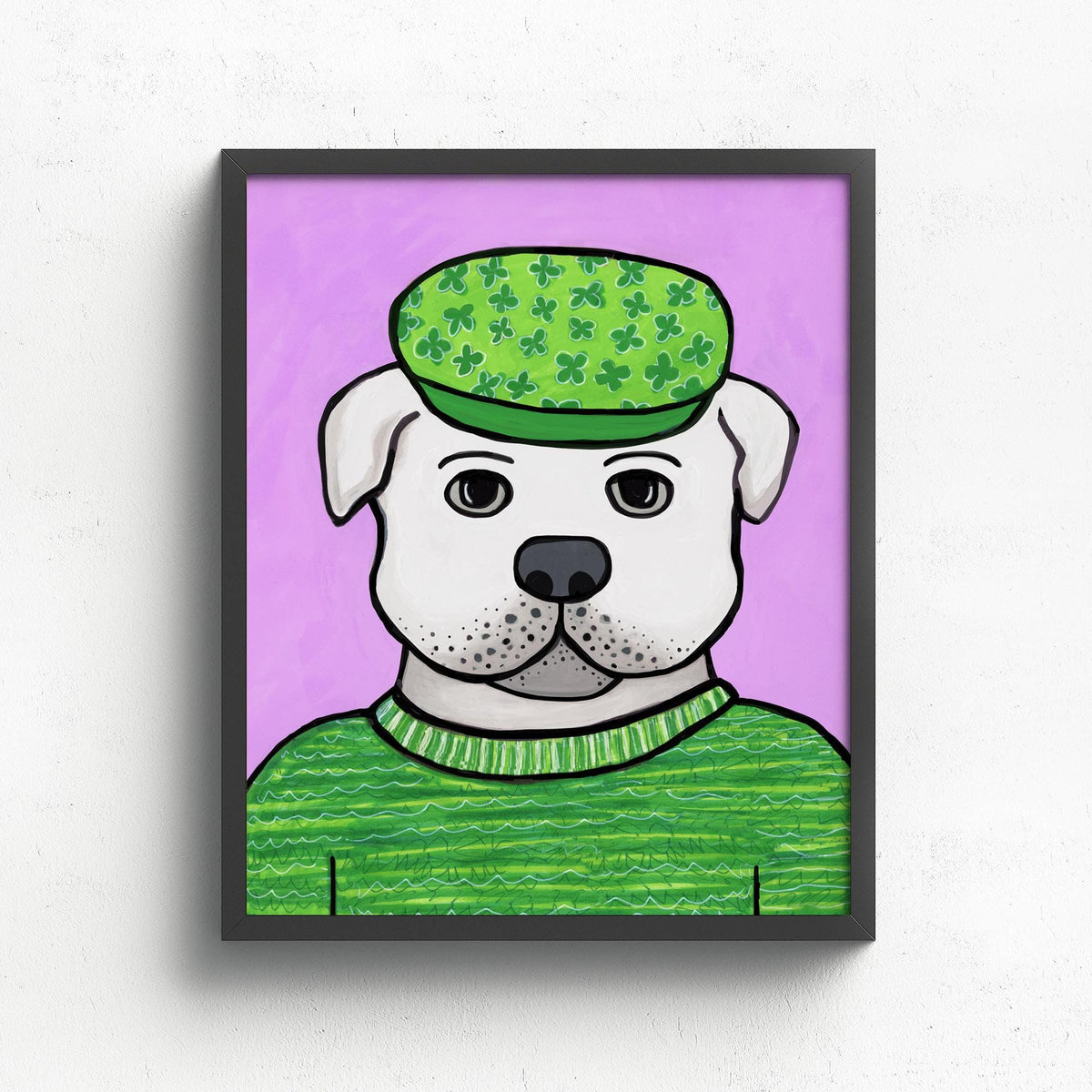 art print featuring a white bulldog in a green sweater and green cap with a light purple background. shown in a black frame on a white wall.