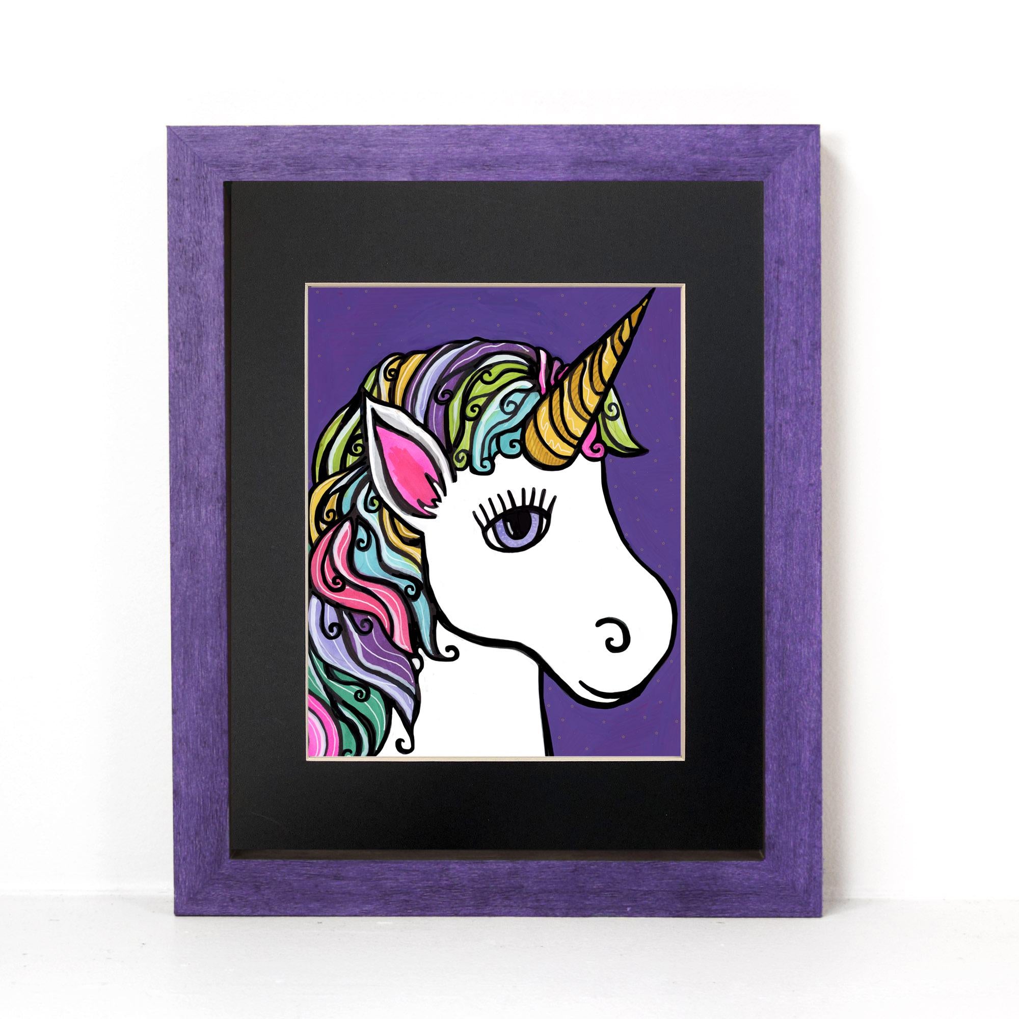 Unicorn art print shown in a purple frame with black matte on a white wall. The unicorn is shown in profile with rainbow hair on a purple background with tiny starts.