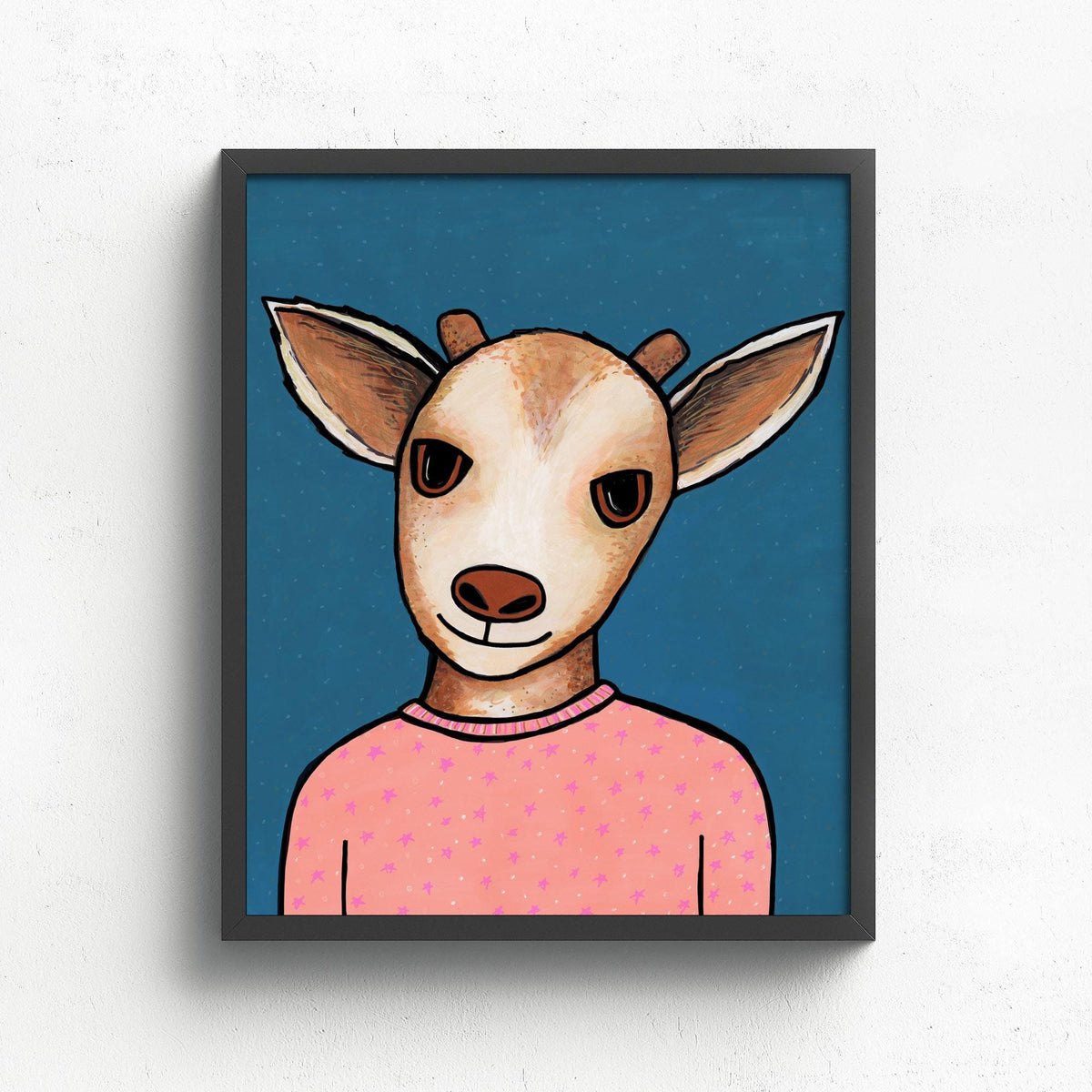 Goldie Goat art print in a black frame on white wall. The art features a brown and white young goat in peach pajamas with little stars and dots on a blue background with subtle dots.