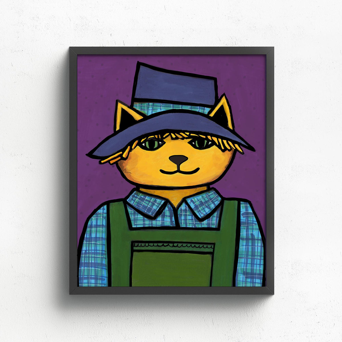 Scarecrow Cat art print shown in a black frame on a white wall. The cat is yellowy orange in a blue hat, green overalls, and blue plaid shirt on a purple background.