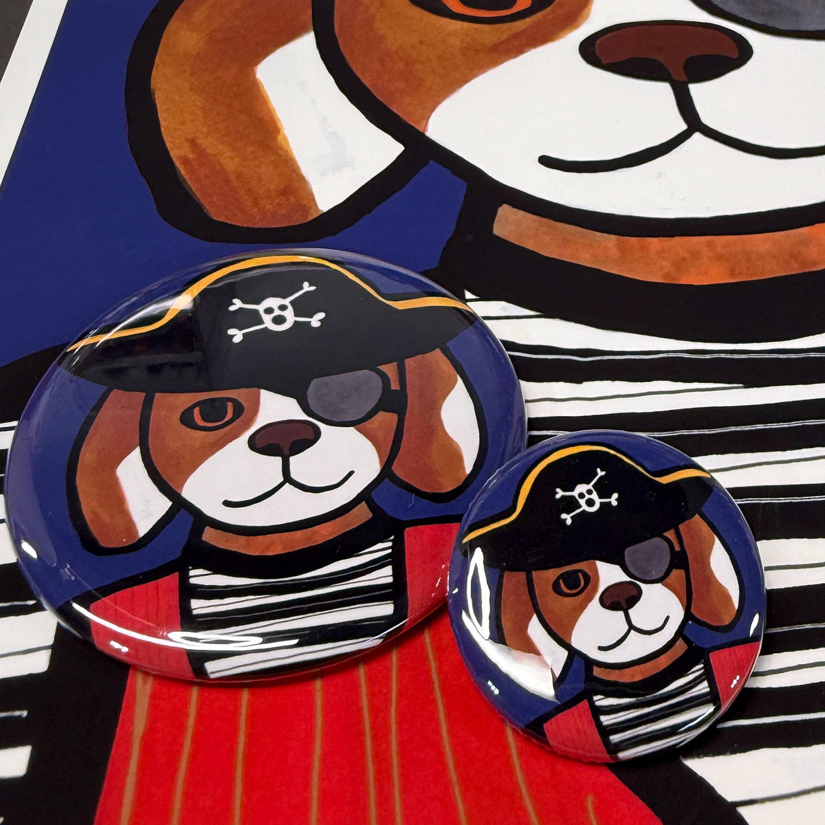 Pirate Dog buttons shown on a print of Pirate Dog.  Pirate Dog is wearing a black and white striped shirt, red vest, eye patch and skull and cross bones hat.
