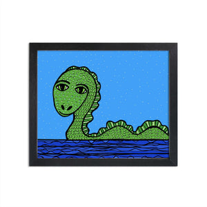 Loch Ness Monster art print in a black frame on a white wall - green sea serpent looking towards the viewer with larger eyes and snake like body rising from the water. Background is a lighter blue wth white dots.