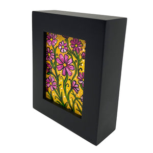 Side view of black wood frame holding pink cosmos flower painting. Flowers and green leaves are on a yellow ochre background.