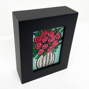 Side view of Vase of Roses painting in black frame - White striped vase with red roses and green leaves. Light blue background with white polka dots.