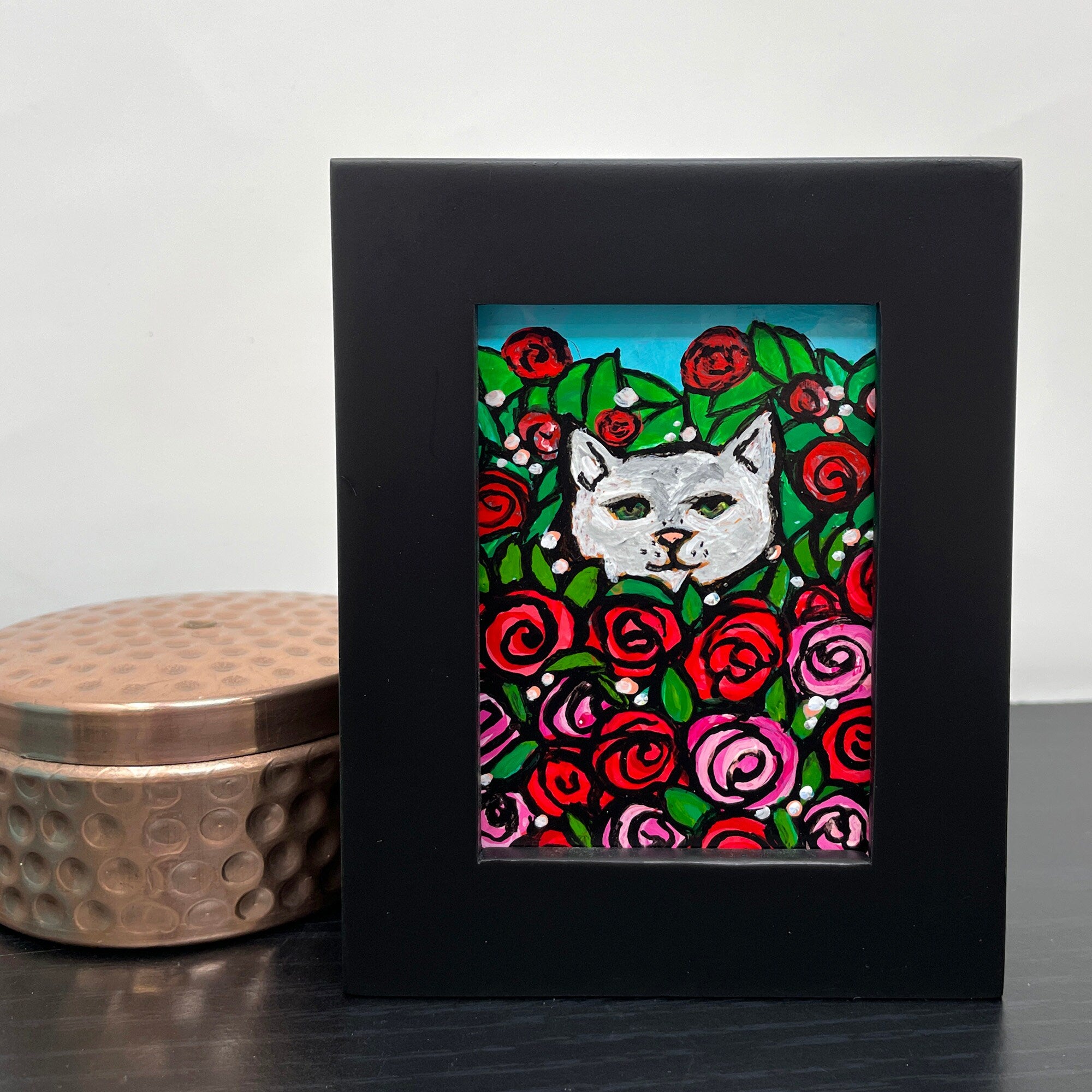 Rose Kitty II painting sitting next to copper trinket box on black table