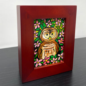 Side view of small framed acrylic painting of a brown barred owl surrounded by pink apple blossoms and green leaves